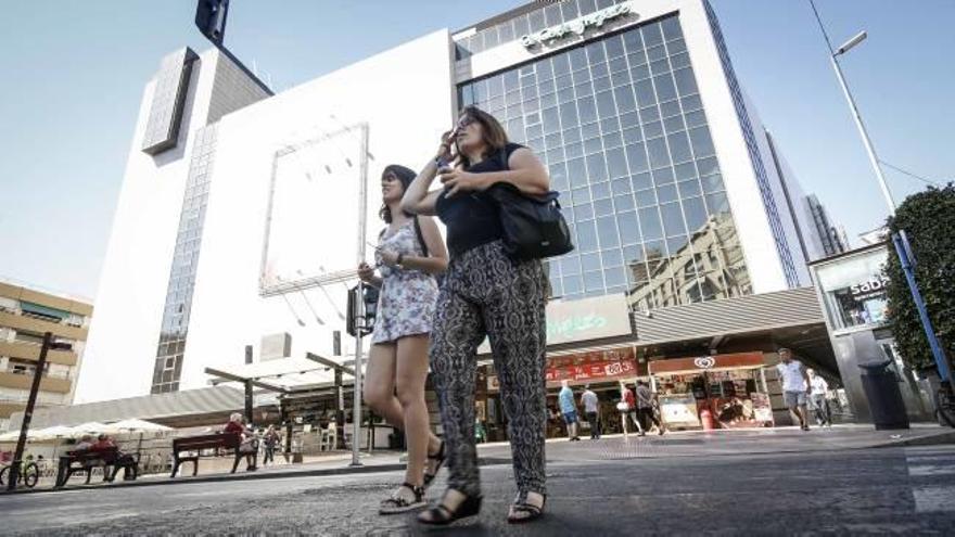 Dos mujeres, en primer plano, caminan frente a El Corte Inglés, en la comercial avenida Maisonnave de la ciudad de Alicante.