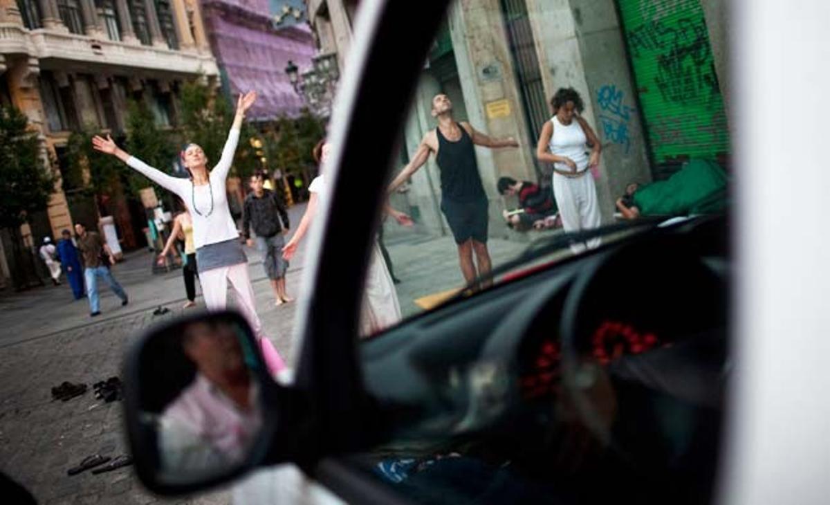 Un conductor espera a l’interior del seu vehicle a la Puerta del Sol davant un grup d’indignats que practiquen ioga.