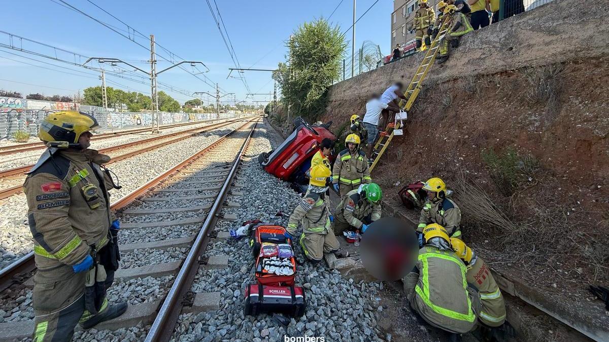 Els Bombers, treballant en el rescat dels ocupants deo cotxe caigut a la via