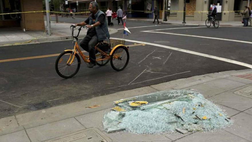 Un ciclista pasea junto a una montaña de cristales recogidos por voluntarios que limpian las calles.
