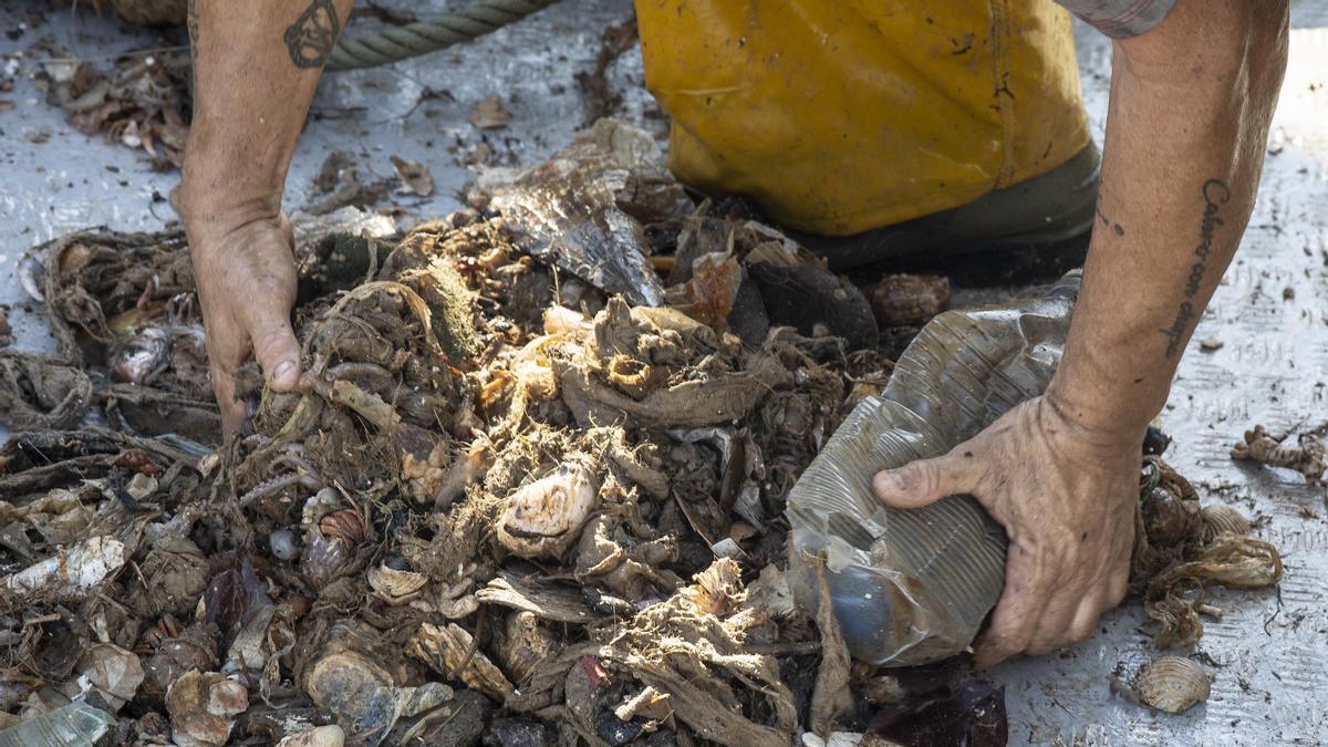 Un pescador recoge una red llena de residuos plásticos.