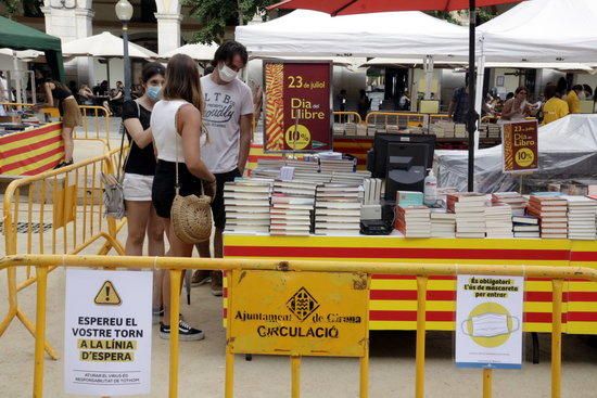 Cartells recordant que l'ús de mascaretes és obligatori davant una parada de llibres a Girona.