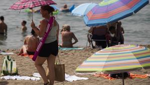 Una mujer con una sombrilla buscando sitio en una playa de Málaga