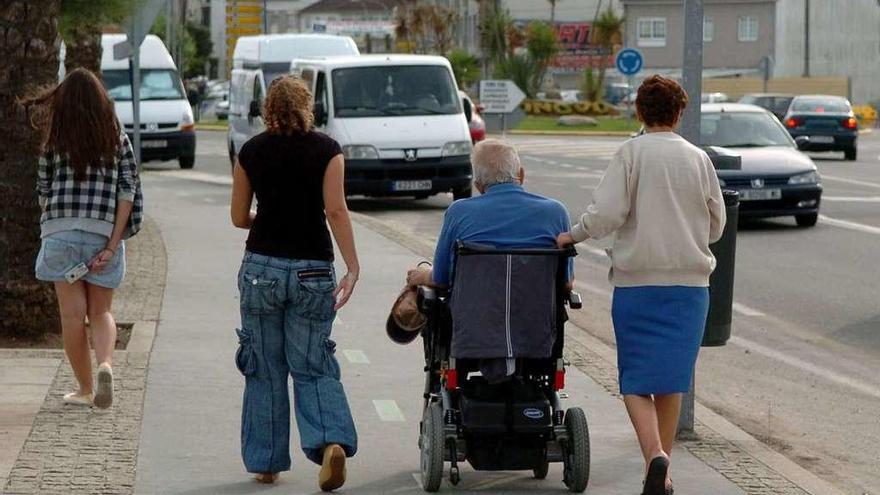 Dos mujeres acompañan a un hombre de avanzada edad en silla de ruedas. // Gustavo Santos