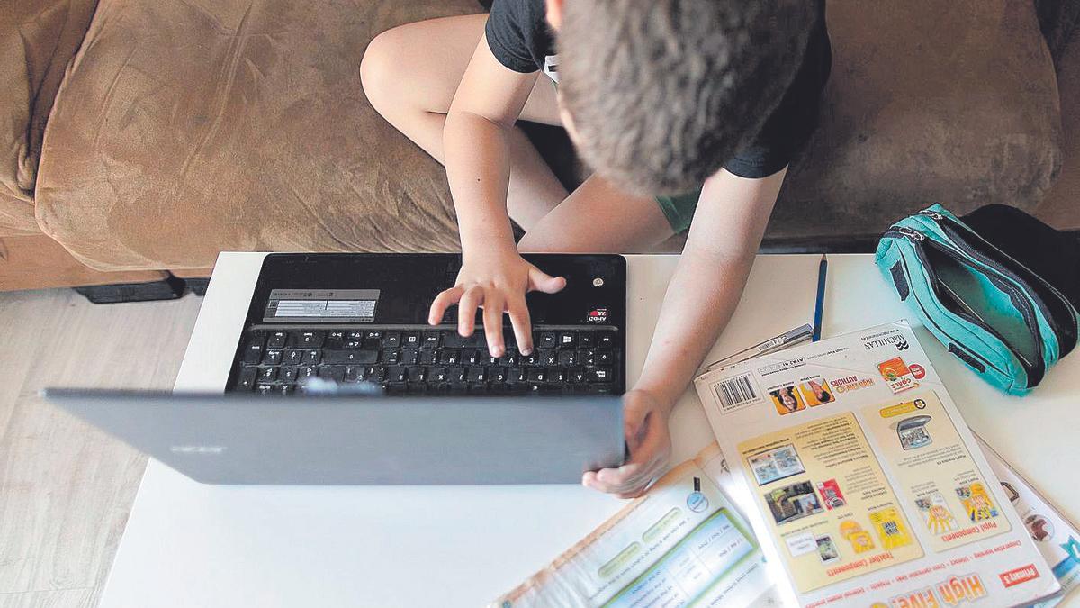 Un niño consulta su portátil mientras realiza tareas de inglés en su casa.
