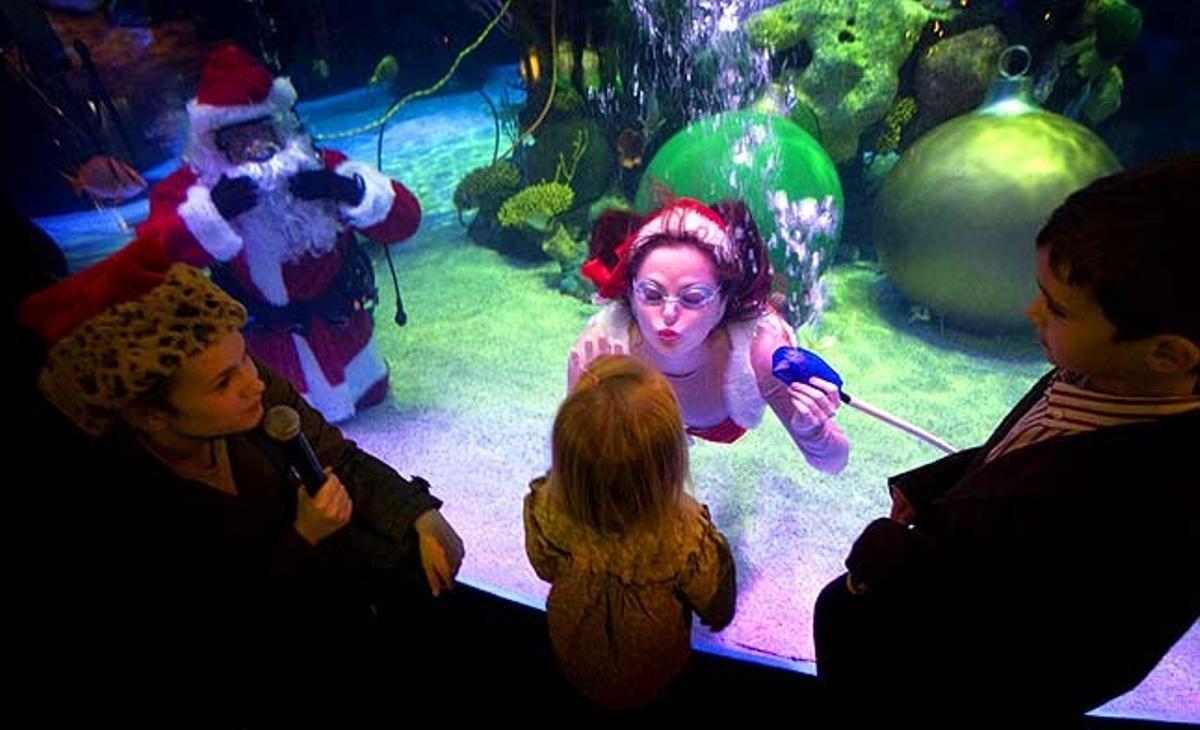 Una dona disfressada d’ajudant de Pare Noel llança un petó sota l’aigua a una nena en una visita a l’aquari de l’hotel i casino Silverton a Las Vegas, Nevada (Estats Units).