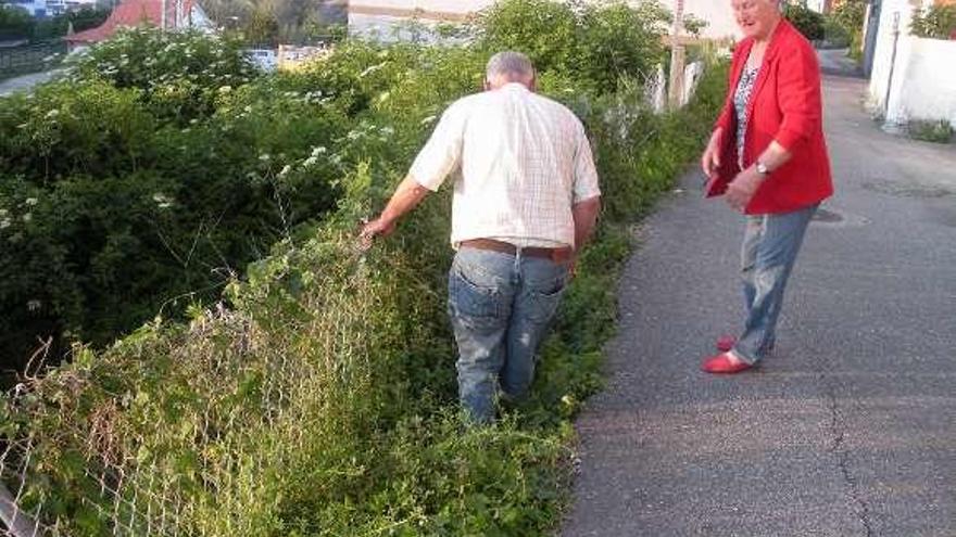 Unos vecinos muestran el mal estado en que se encuentra la valla que protege del talud en el Camiño Real Angorén. // FdV