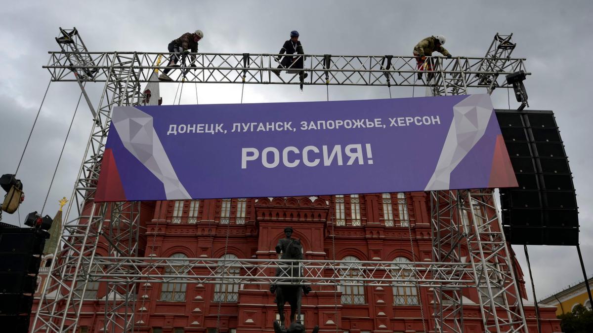 Varios trabajadores colocan un cartel en el que se lee &quot;¡Donetsk, Lugansk, Zaporiyia, Jersón son Rusia!&quot; en lo alto del escenario instalado en la plaza Roja de Moscú para la celebración de este viernes.