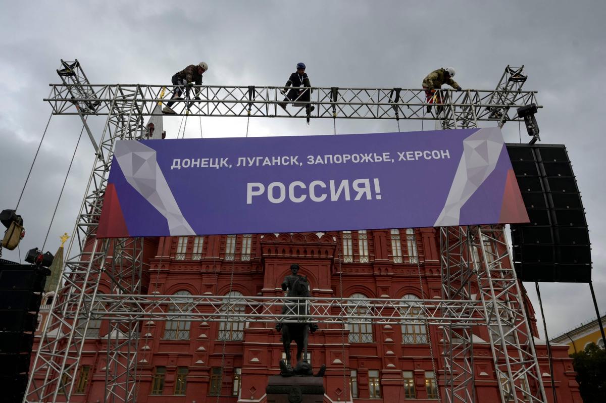 Varios trabajadores colocan un cartel en el que se lee &quot;¡Donetsk, Lugansk, Zaporiyia, Jersón son Rusia!&quot; en lo alto del escenario instalado en la plaza Roja de Moscú para la celebración de este viernes.