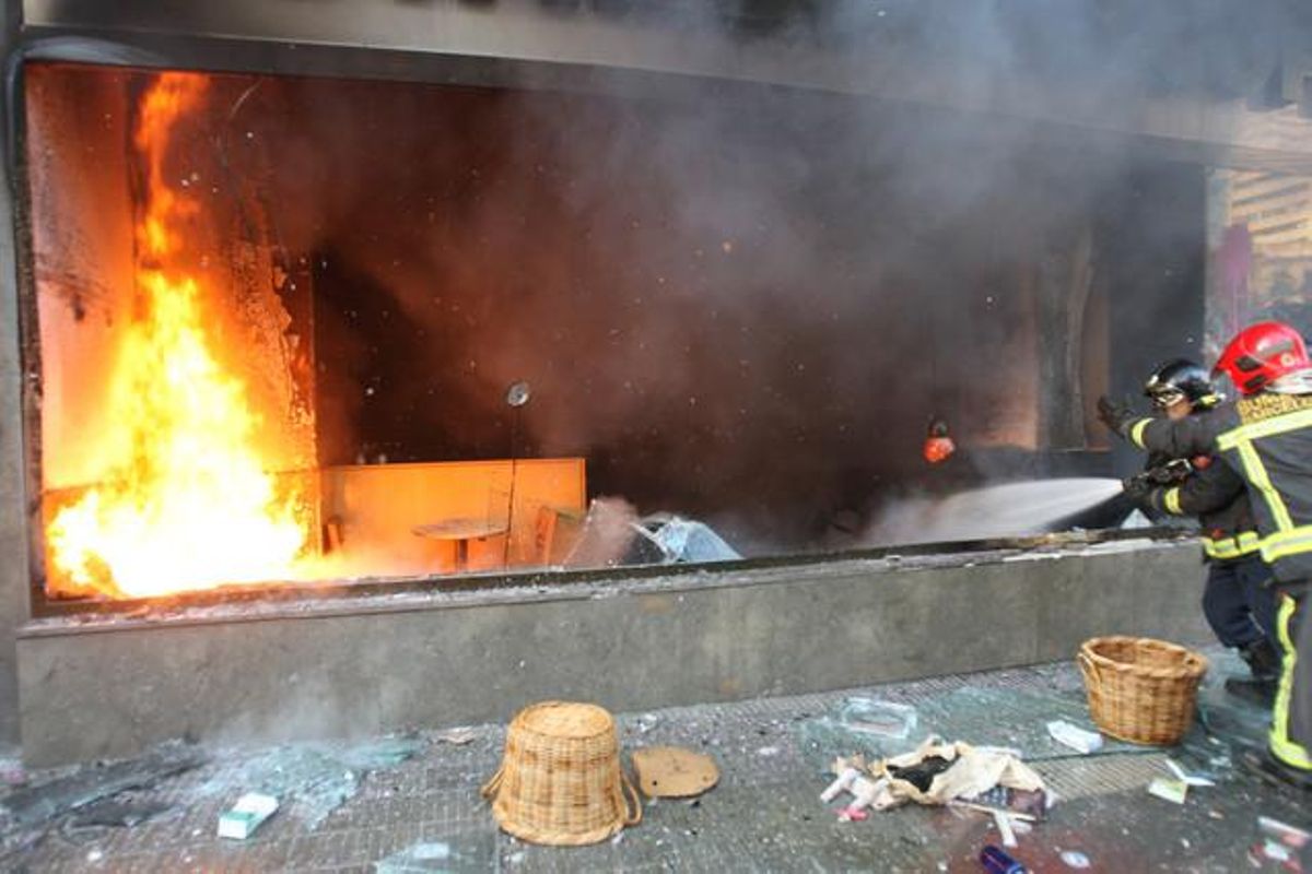 Los bomberos intentan apagar el incendio del escaparate de un comercio del centro de Barcelona.