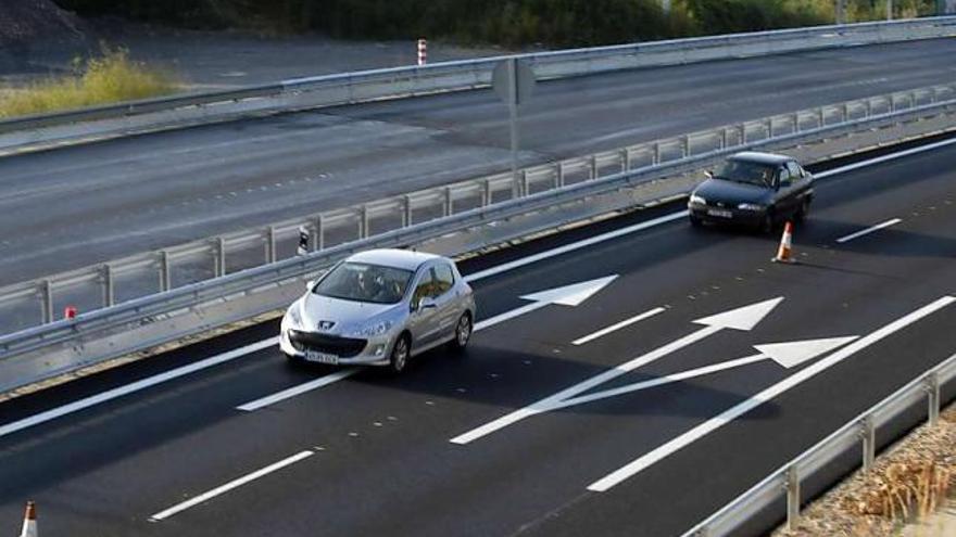 Dos coches circulan por la calzada ya terminada; a la otra le faltan los últimos retoques.