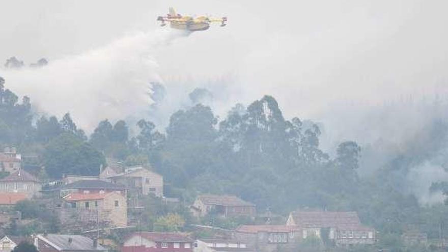 Un avión descarga agua en un incendio cerca de unas casas. // G. S.