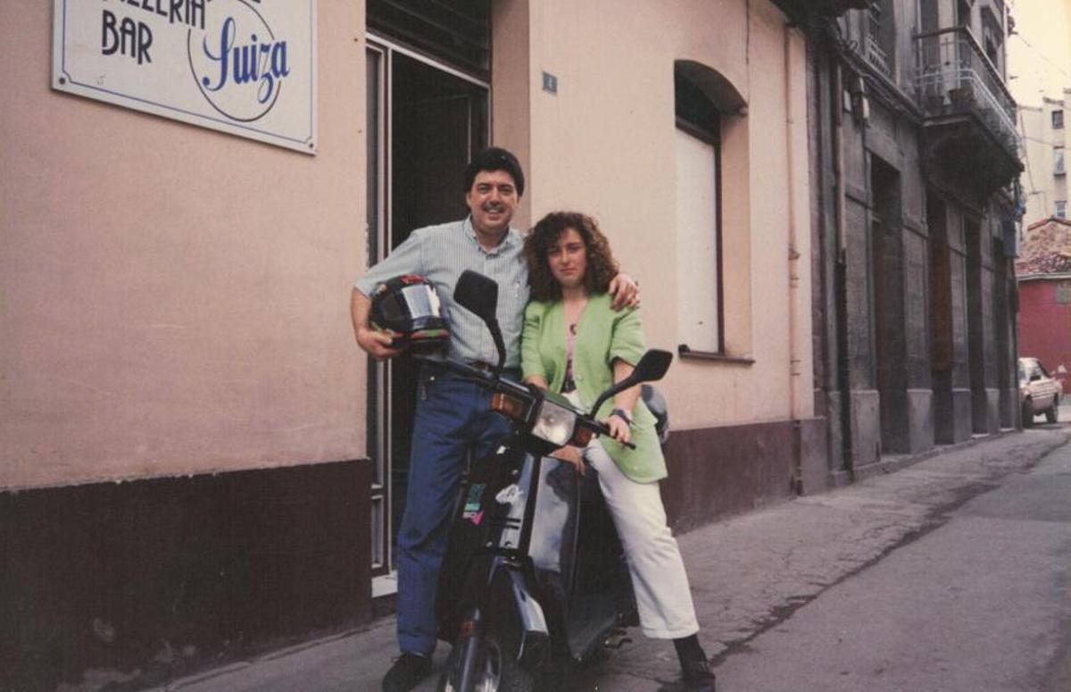 Ana Belén Estremador, y su padre, Carlos, con la primera moto de reparto, en 1992, ante el establecimiento.