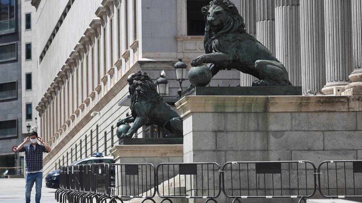 Un hombre coloca mascarilla mientras camina delante fachada Congreso Diputados