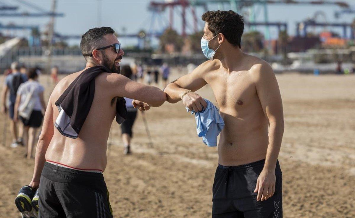 Dos jóvenes se saludan con el codo en la playa de Valencia.