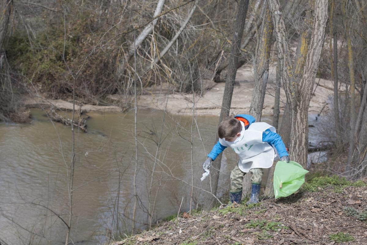 Un niño recoge basuraleza junto a un río.