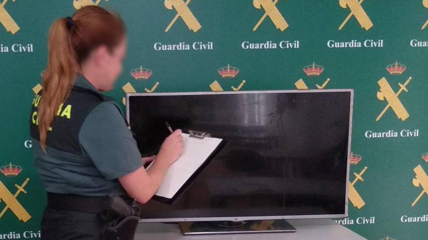 Una guardia civil junto al televisor robado por los detenidos.