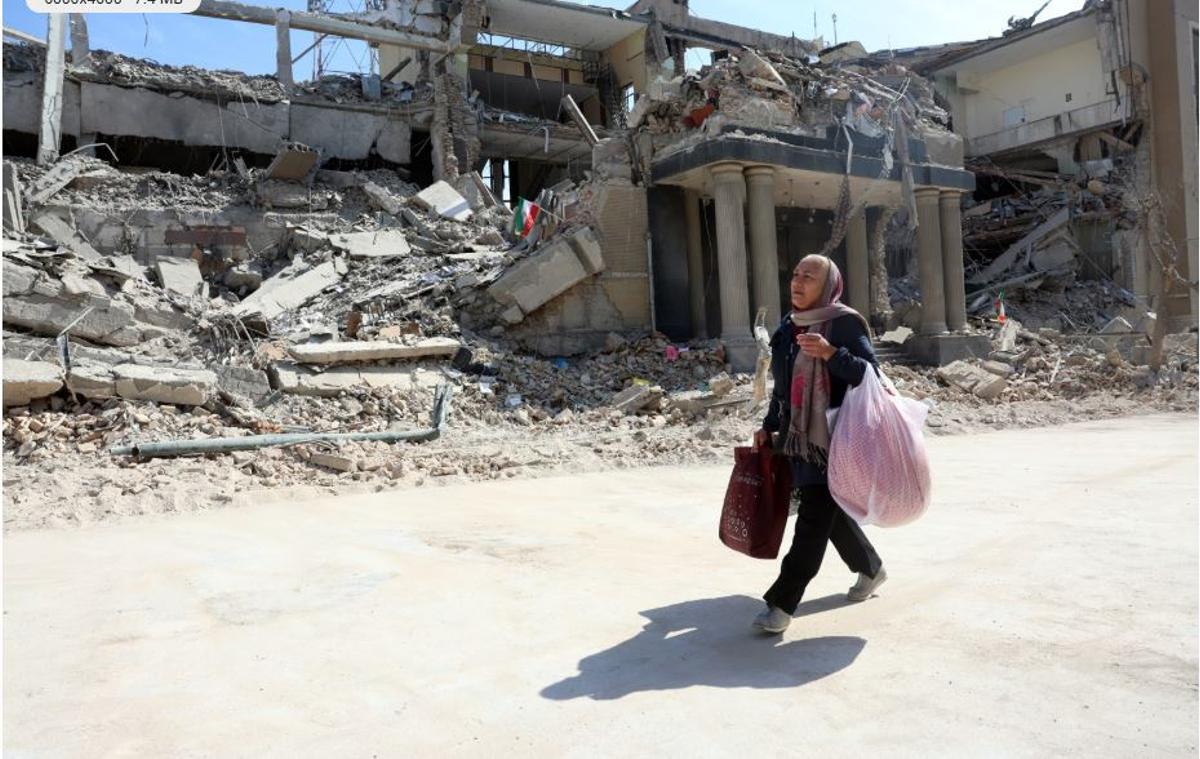 Una mujer camina junto a un edificio en ruinas por las bombas en Teherán.