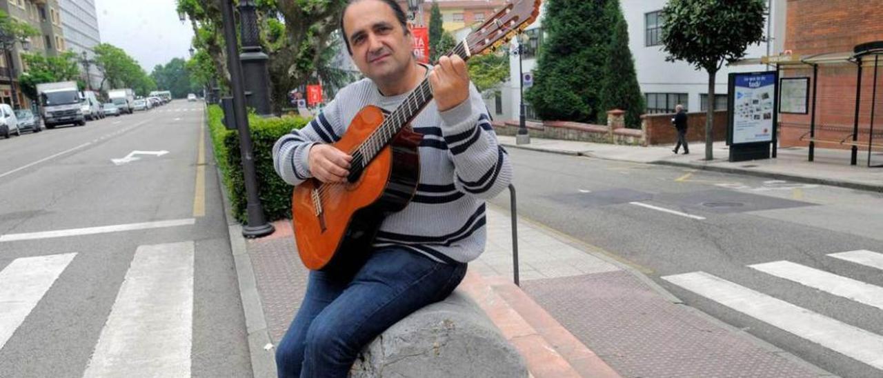 Fernando Corujo toca la guitarra sentado en el hito del kilómetro cero, en Arzobispo Guisasola, frente a las Escuelas Blancas.