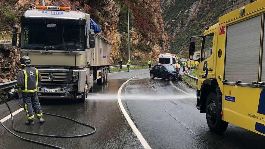 Los bomberos, ayer, limpiando la carretera junto al camión y el coche accidentados, en Calabazos.