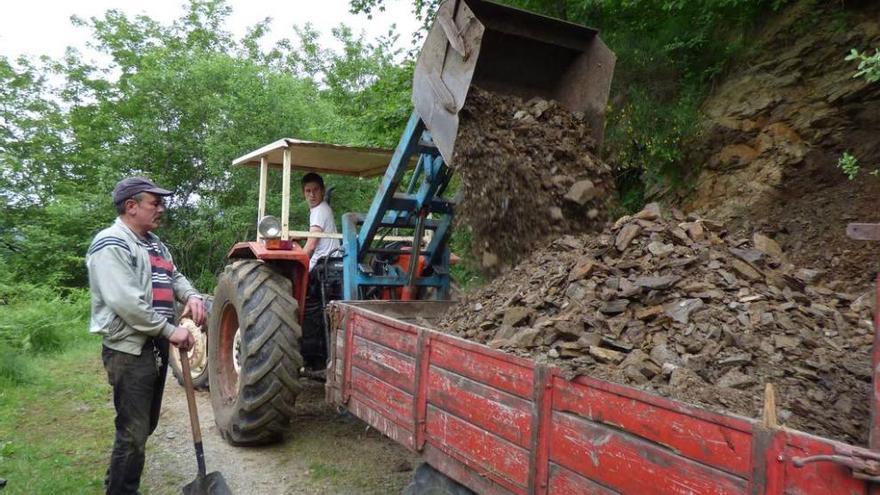 Jorge Díaz carga escombro en el tractor de Manuel Rodríguez. A la derecha, Manuel Antón Caballero rastrilla el relleno de los baches.