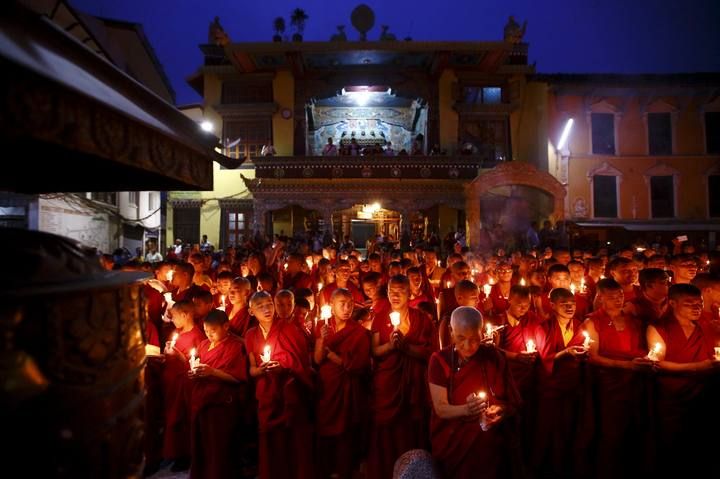 Buddhist monks holding candles offer prayers for the victims of earthquakes in Kathmandu
