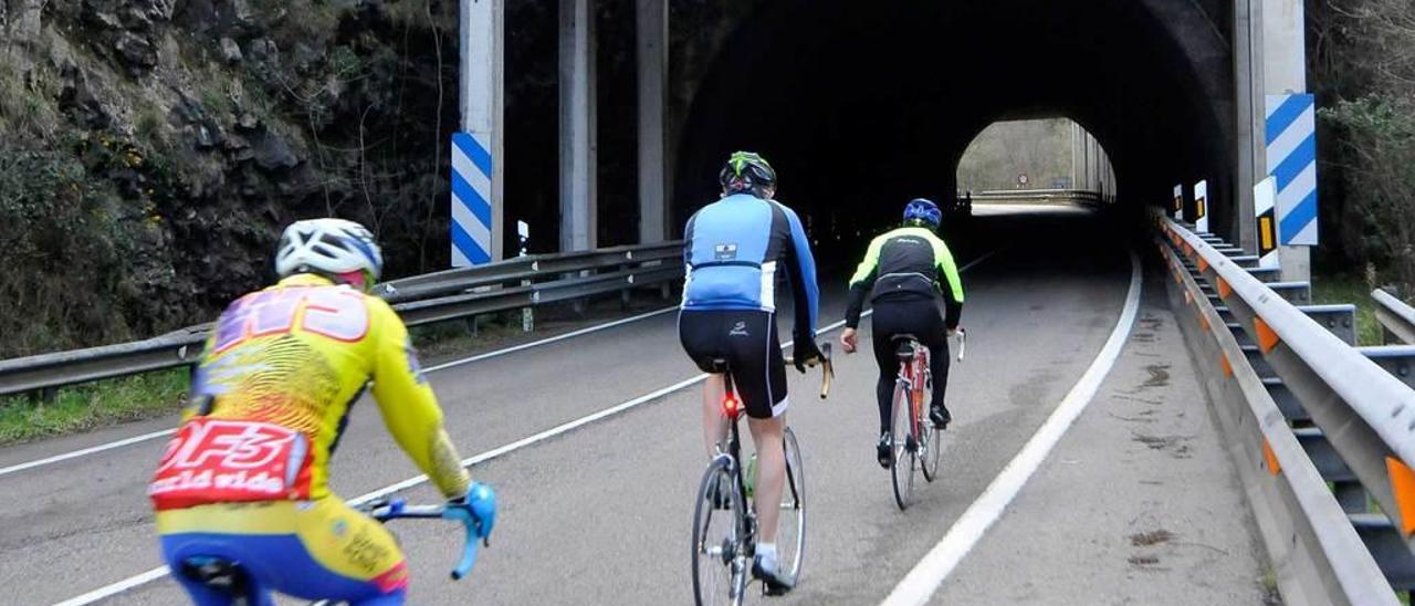 Tres ciclistas transitan por uno de los túneles de la vieja carretera nacional 630 de Mieres a Oviedo.