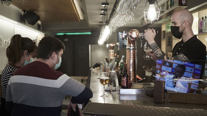 Un camarero y unos clientes, con mascarilla en el interior de un bar.