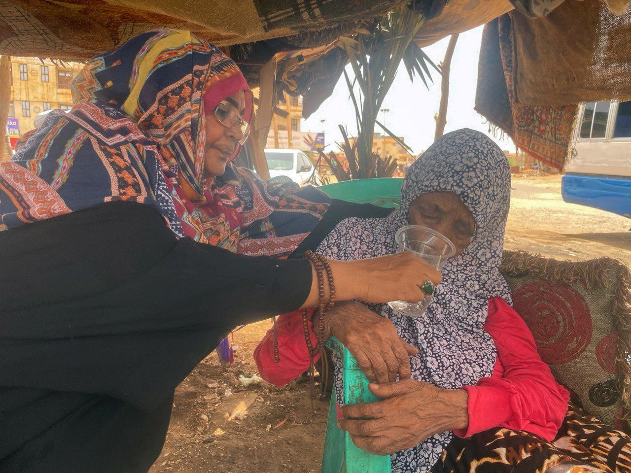 Una mujer ayuda a otra a beber agua bajo una carpa en la que se refugian durante una parada en su huida de los combates en Jartum, la capital de Sudán, este martes.