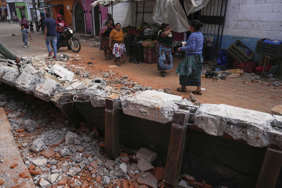 Residents walk past debris from damaged houses in Santa Maria de Jesus, Guatemala, Wednesday, July 9, 2025, following dozens of earthquakes and aftershocks that were recorded in a matter of hours. (AP Photo/Moises Castillo). EDITORIAL USE ONLY/ONLY ITALY AND SPAIN