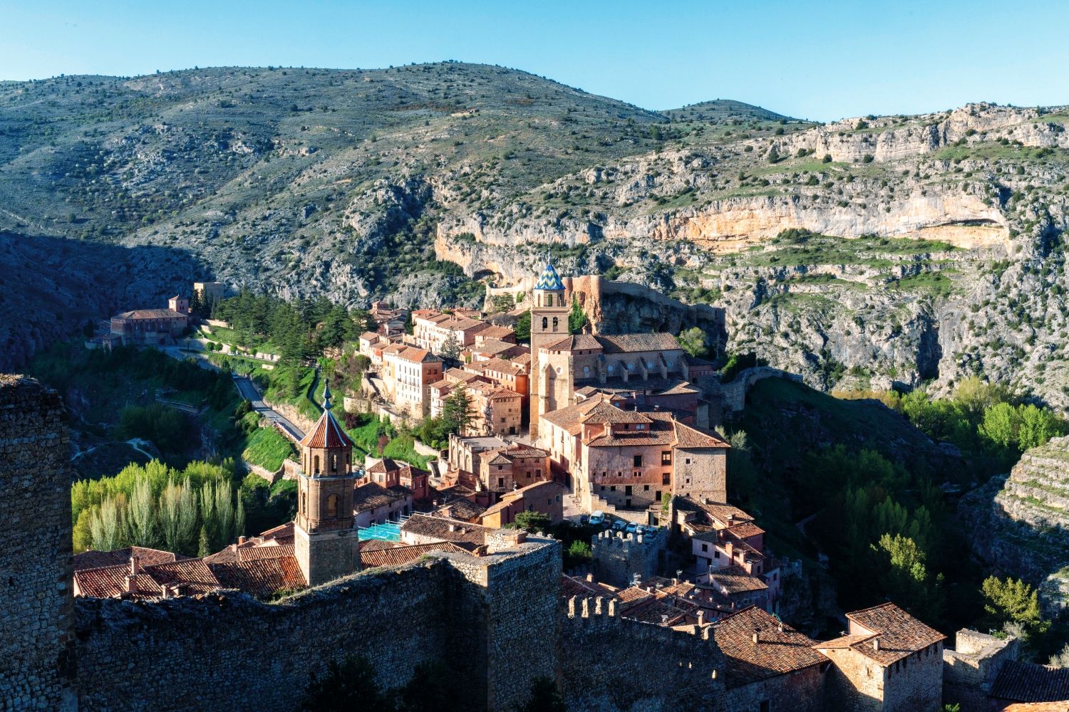 Vista de Albarracín con su muralla medieval, que asciende por la ladera hasta la Torre del Andador. Esta fortificación, iniciada en el siglo X por los Banu Razin y ampliada en épocas posteriores, refleja la importancia estratégica de la ciudad durante la Edad Media. En tiempos del Cid, Albarracín era la capital de una taifa independiente, que en 1088 se convirtió en tributaria del Campeador tras negociaciones en Calamocha.
