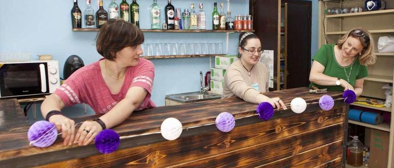 Marisol Riera, Demelsa Riera y María José Pérez colocan unas guirnaldas para la fiesta.