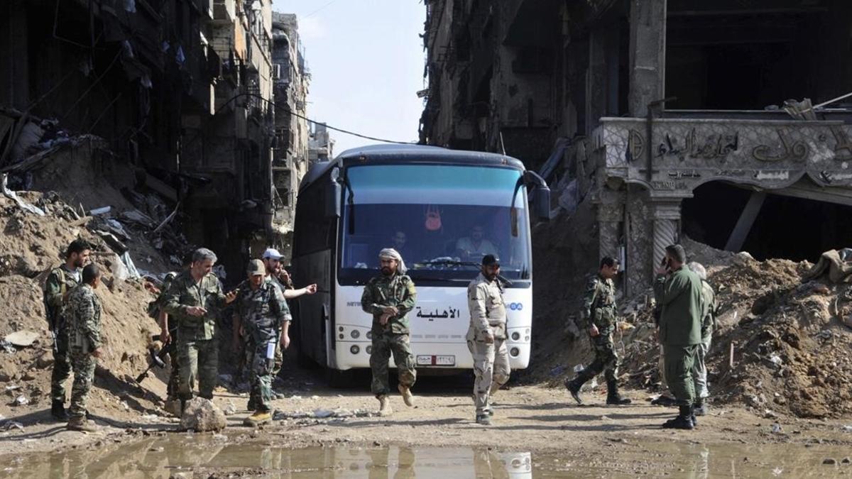 Militares del Ejército sirio supervisan un autobús que transporta combatientes vinculados a Al Qaeda durante una evacuación desde el campo de refugiados palestinos de Yarmuk, cerca de Damasco.