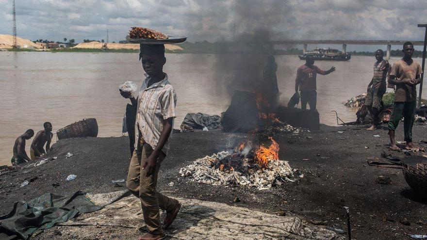 Un niño pasa frente a un punto donde queman basura y materiales de caucho en Yenagoa (Nigeria).