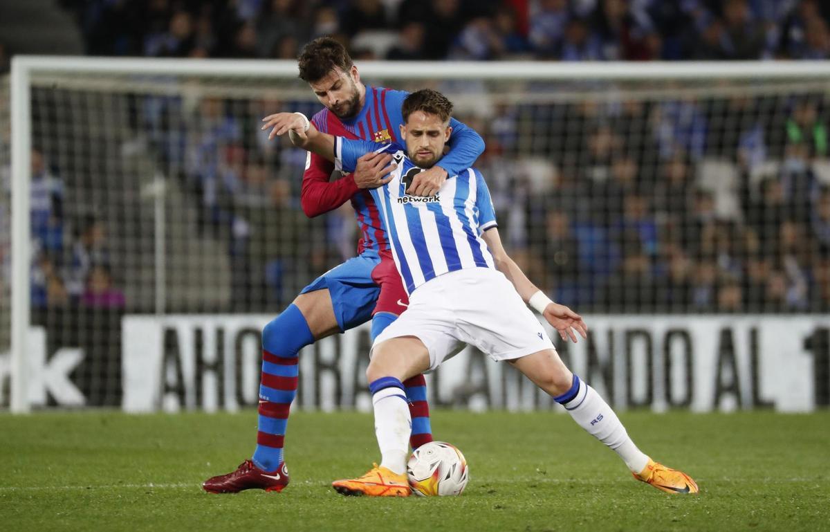 SAN SEBASTIÁN, 21/04/2022.- El centrocampista belga de la Real Sociedad, Adnan Januzaj, protege el balón ante el defensa del FC Barcelona, Gerard Piqué, durante el encuentro correspondiente a la jornada 33 disputado hoy jueves en el Reale Arena de San Sebastián. EFE / Juan Herrero.