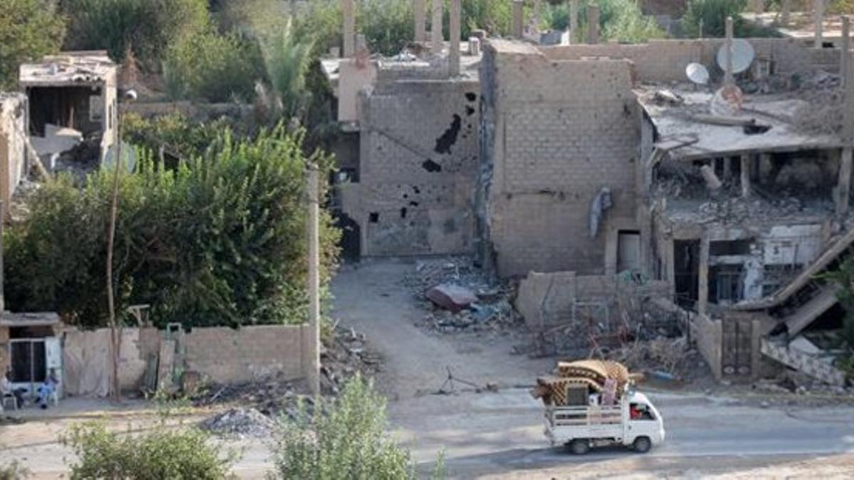 Una 'pick-up' circula junto a edificios destruidos en Deir Ezzor, en el este de Siria, este lunes.