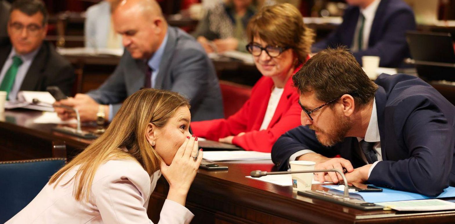 La presidenta Marga Prohens habla con Sagreras en el Parlament y, detrás, Vicent Marí consulta su teléfono. | TOMÀS MOYÀ