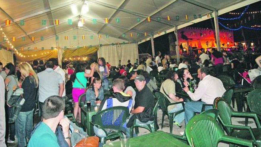 Arriba, decenas de personas, disfrutando de la carpa instalada en  el aparcamiento de  Perán. A la izquierda, dos mujeres se afanan en los preparativos del reparto del bollo.