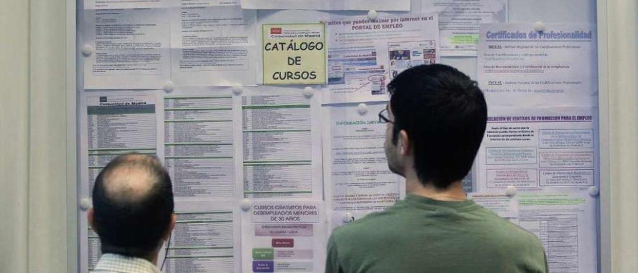 Dos trabajadores de distintas edades, frente a un tablón de anuncios en una oficina del Inem. // A. Comas