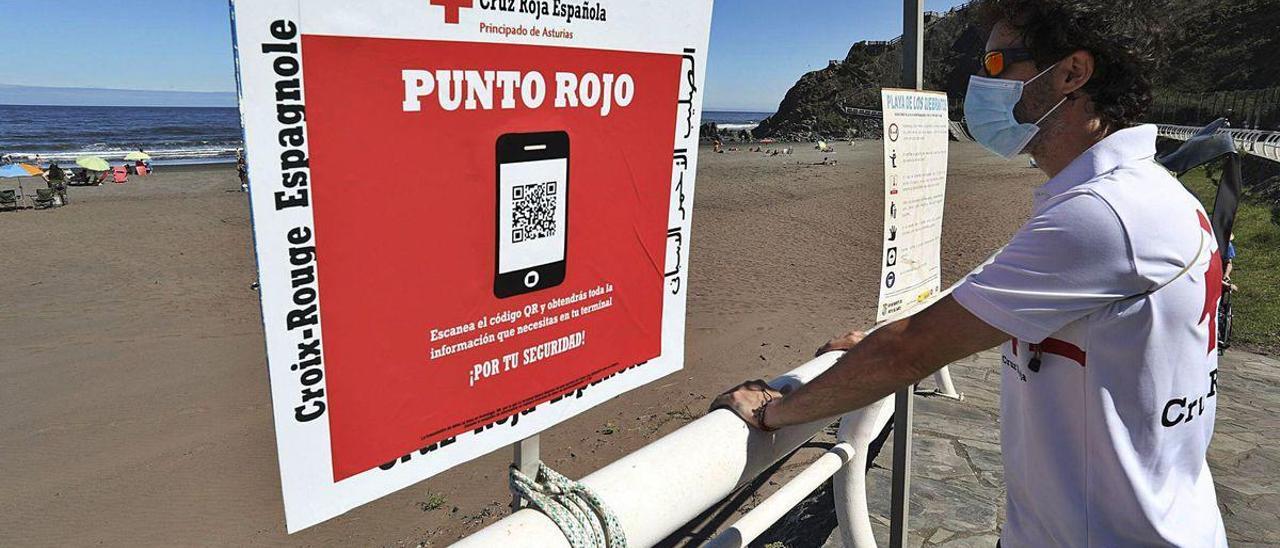 Álvaro Aristegui, junto al cartel que permite a los bañistas de Los Quebrantos acceder con la lectura de un código QR a información sobre la prevención de contagios por covid.
