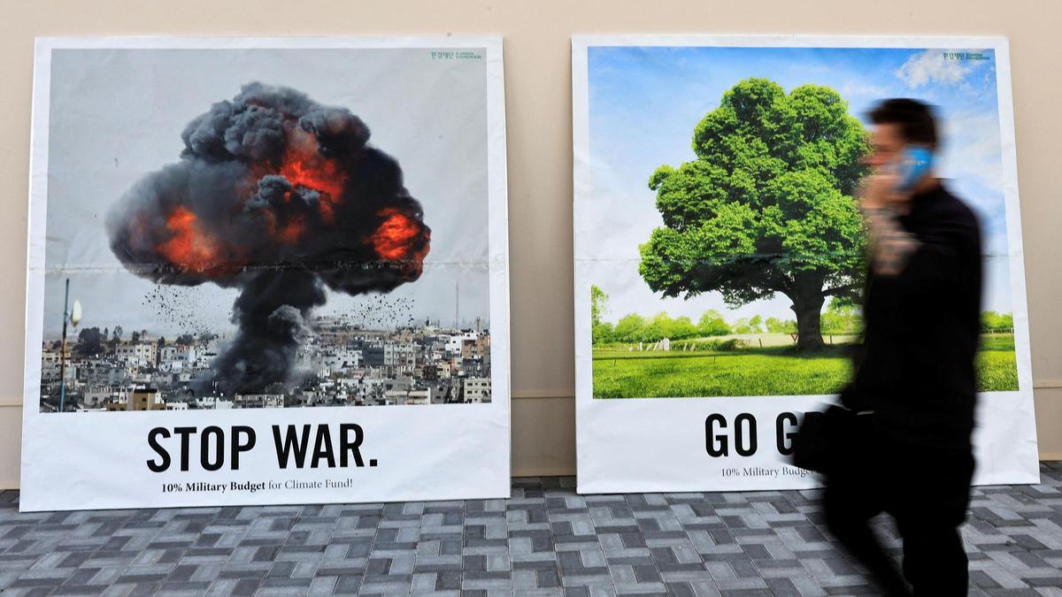 Un hombre pasa junto a un muro con dos pancartas que dicen &quot;Stop war&quot; y &quot;Go green&quot; en la Conferencia de las Naciones Unidas sobre el Cambio Climático (COP28) en Dubai.