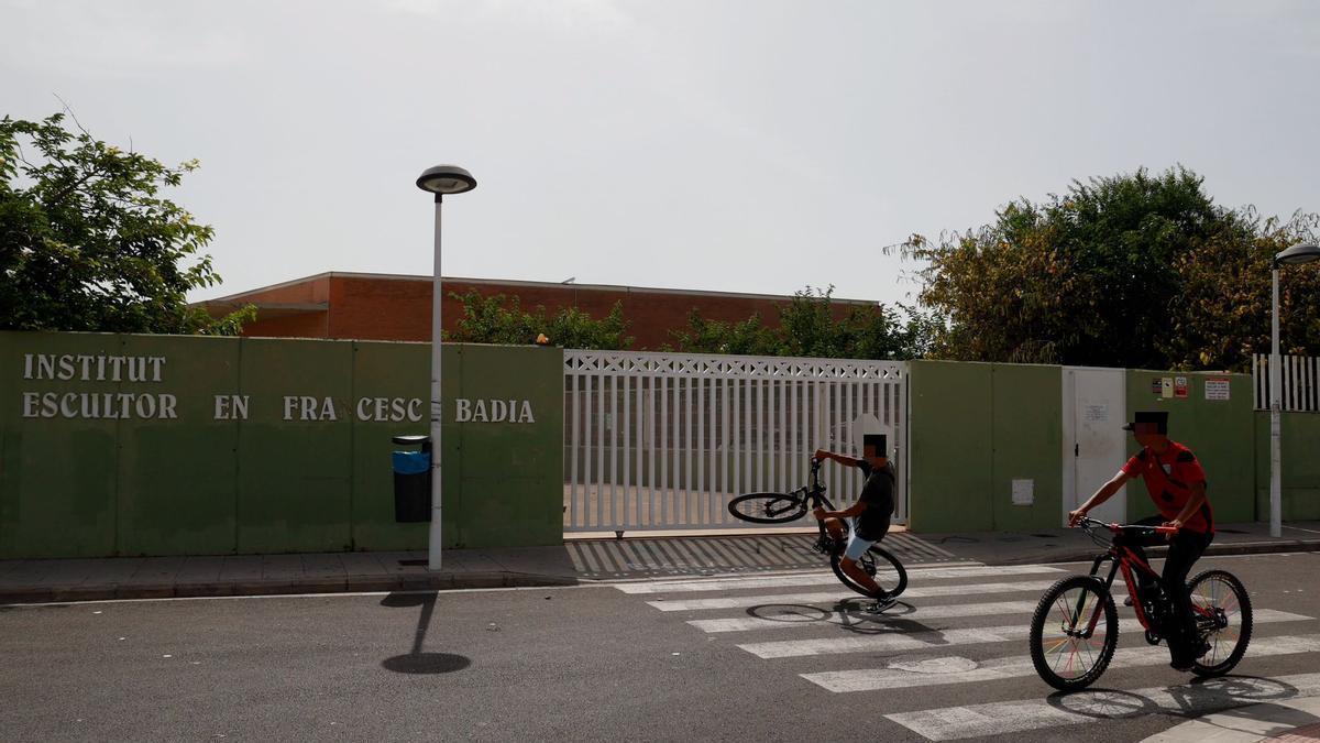 Dos adolescentes, en bici, pasan justo por delante de la puerta del IES de Foios