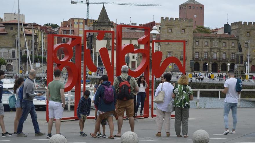 Turistas haciéndose fotos ante las &quot;letronas&quot;, en el Puerto Deportivo de Gijón, con Cimadevilla al fondo.