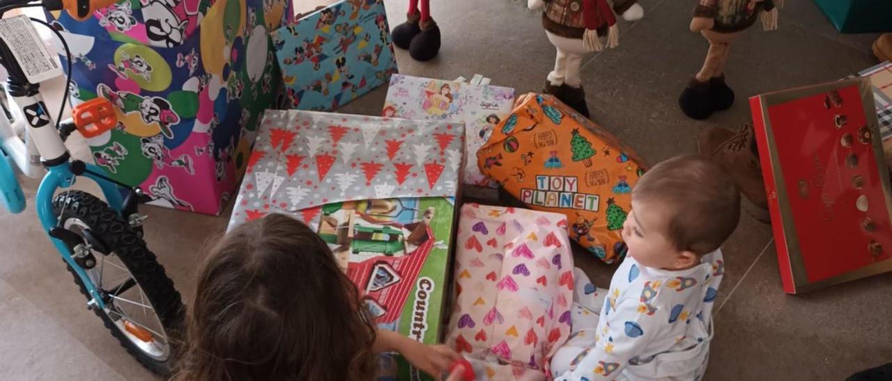 Dos niñas abren sus regalos el día de Reyes, junto al árbol de Navidad. | Cedida