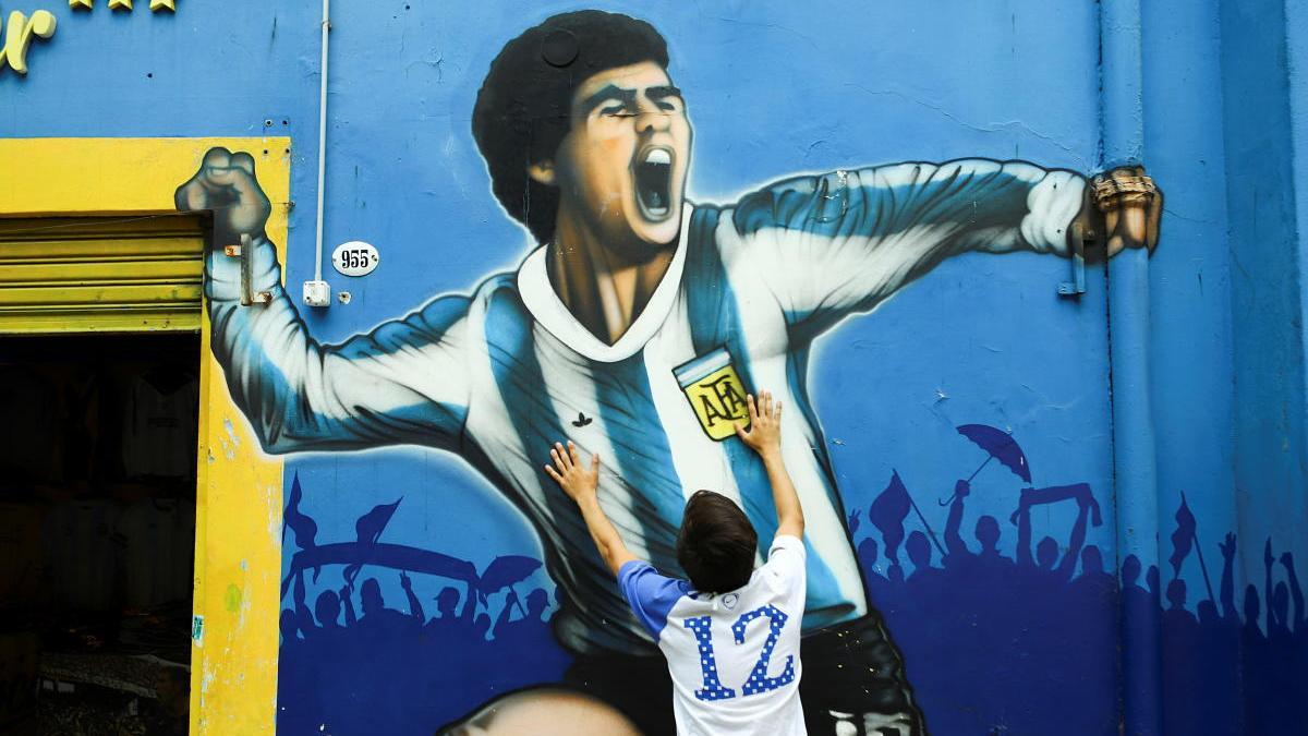 Un fan toca un retrato de Maradona pintado en una pared de Buenos Aires.