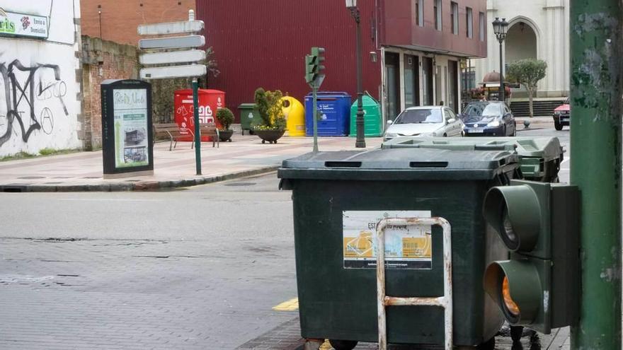 En primer término, dos contenedores en la calle Isabel la Católica de Sama, con un minipunto limpio y depósitos de reciclaje al fondo.