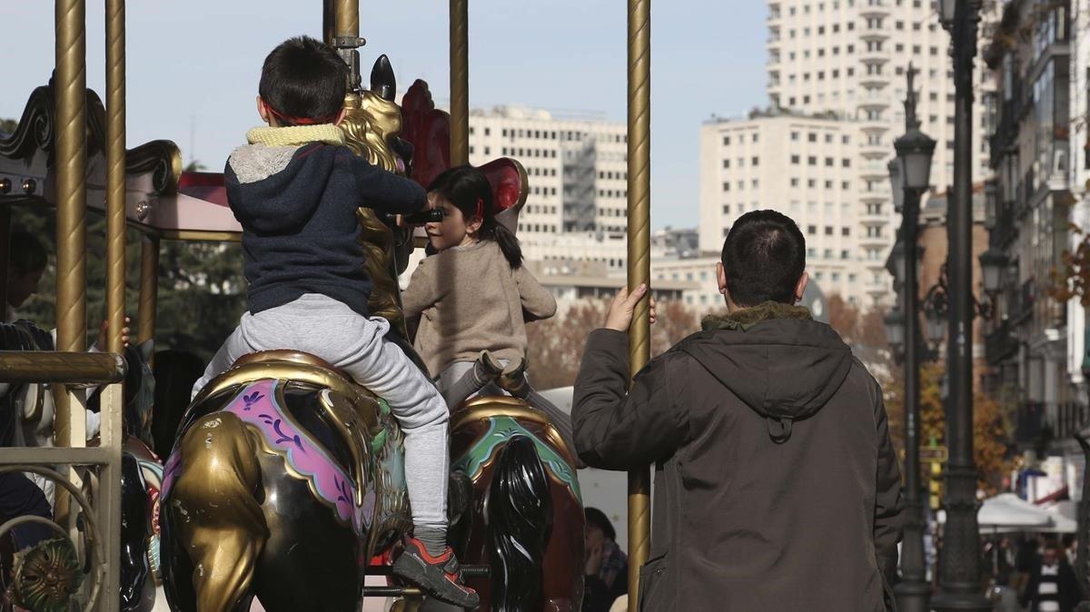 Unos niños montan en un tiovivo en presencia de adultos, en Madrid.