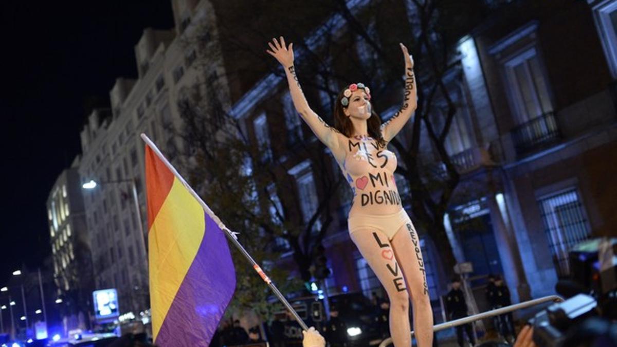 Una mujer con mensajes escritos sobre su cuerpo saluda a los otros manifestantes, durante la protesta que ha tenido lugar en los alrededores del Congreso de los Diputados este sábado, en Madrid