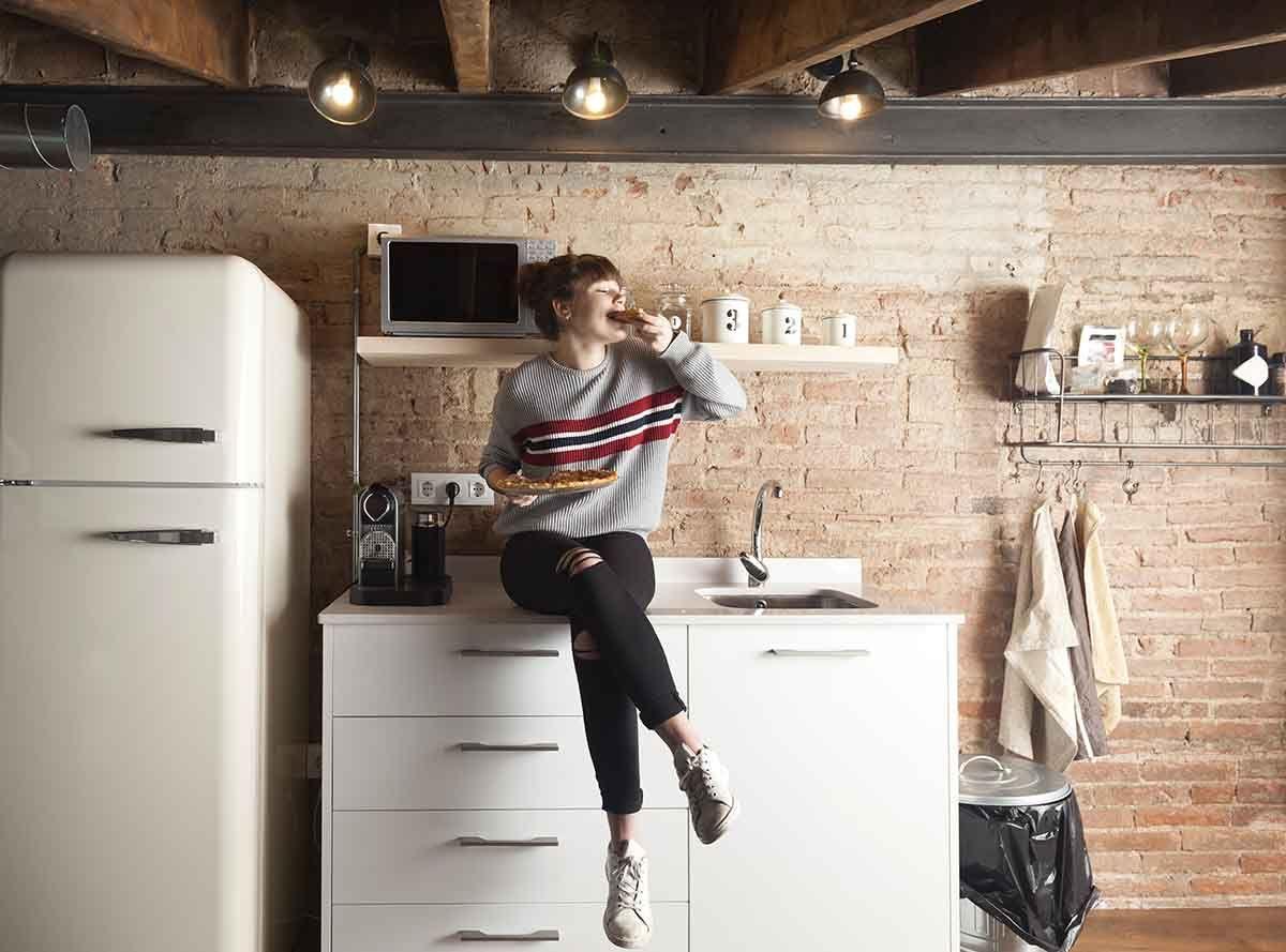 Mujer comiendo una pizza en la cocina de su casa