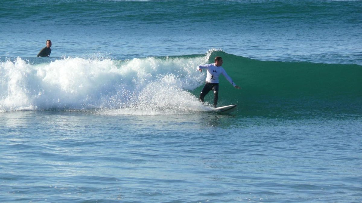 Andrés Campos surfeando bajo la inspección de Kevin, a sus espaldas